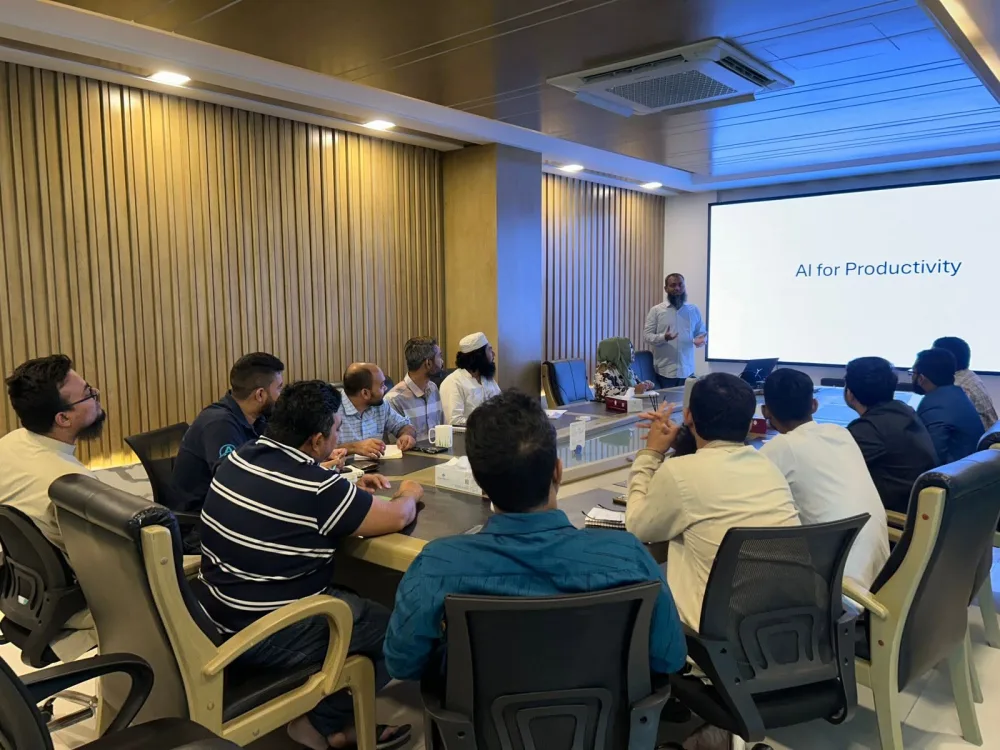 A trainer presenting an "AI for Productivity" slide to a dozen participants seated around a boardroom table