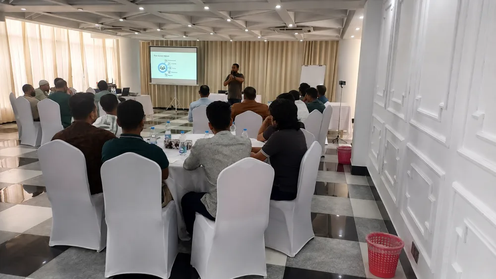 Participants seated at round tables in a hotel training hall, watching a projected slide on the five Scrum values